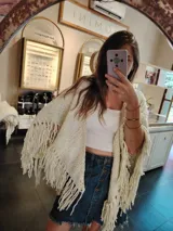 Ruana triangular tejida a crochet color crema con flecos largos.