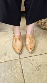 Zapatos destalonados de cuero color tostado, con perforaciones en el empeine y cierre lateral con hebilla metálica.