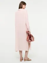 Camisa larga de corte oversize, color rosado, con cuello camisero, cierre frontal con botones y mangas largas.