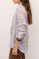 Camisa de seda color celeste y beige, con estampado de hojas en tonos azules, cuello camisero, manga larga y cierre frontal de botones.