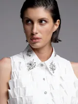 Camisa blanca sin mangas con cuello clásico, cierre frontal con botones y apliques de strass en cuello y frente.