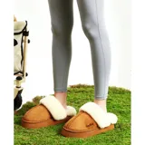 Pantuflas de gamuza color beige con plataforma y forro interior de corderito sintético. Presentan un diseño sin talón con el nombre de la marca bordado en el lateral.