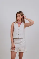 Chaleco sastrero de diseño estructurado, confeccionado en tela blanca con sutiles bordados florales en tonos dorados y crudos. Presenta escote en V, cierre frontal con botones y corte a la cintura.