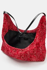 Bolso shopper rojo con estampado tipo bandana y textura plisada. Cuenta con una fina asa de hombro ajustable negra y cierre principal con clip imantado.