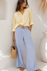 Pantalón palazzo celeste de tiro alto, corte holgado y pernera ancha, con cintura elastizada e incluye un cinturón de rafia trenzada con hebilla circular revestida.