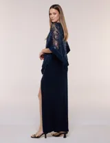 Vestido largo azul marino de seda fría, compuesto por una falda recta con tajo frontal y una capa superior superpuesta de encaje con lentejuelas bordadas, escote a la base y mangas tres cuartos acampanadas.