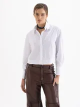 Camisa blanca de poplin de algodón con fit cómodo y largo que cubre hasta debajo de la cintura. Presenta botones ocultos en cartera y puños, y punteras de níquel en el cuello.