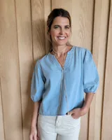 Blusa celeste de mangas 3/4 abullonadas, escote en V con detalle de bordado y lazo decorativo.