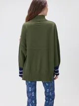 Pullover de punto color rojo, con cuello tortuga, corte holgado y mangas largas con puños acanalados en contraste con rayas blancas. Presenta un logo bordado en el pecho.