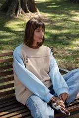 Buzo de corte oversize con diseño color block, combinando paneles en color beige, marrón y celeste. Presenta cuello redondo, mangas largas y un bolsillo frontal con cierre.