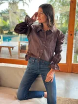 Camisa marrón de algodón con cuello clásico, cierre frontal con botones dorados y mangas largas abullonadas con puños elásticos.