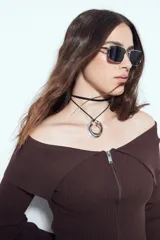 Top de punto acanalado negro, con diseño off-shoulder y escote amplio. Presenta mangas largas y cierre frontal completo con doble cursor, permitiendo ajustar la apertura superior e inferior.