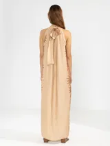 Vestido largo tipo maxi con cuello halter, sin mangas y corte holgado. Presenta un diseño estampado de flores en tonos marrones sobre una base de color beige.