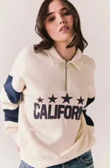 Sweater de algodón color beige claro con cuello polo y cierre frontal parcial. Presenta mangas largas con franjas horizontales azul marino y un estampado frontal con estrellas y la leyenda 'CALIFORNIA'.