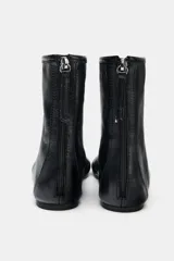 Botín plano de piel color negro, con diseño minimalista, costura central decorativa y cierre lateral mediante cremallera.