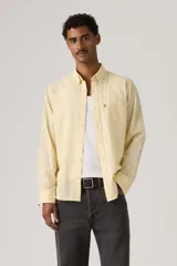 Camisa de manga larga color amarillo claro, con cuello camisero, cierre frontal de botones y un bolsillo aplicado en el pecho con etiqueta roja de la marca.