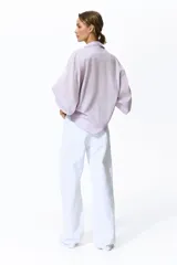 Camisa de algodón color lila, con cuello camisero ribeteado en encaje, cierre frontal de botones con detalles de encaje a los lados y mangas globo largas con puños elásticos.