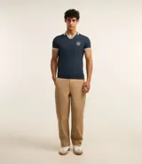 Remera polo comfort color crudo, de manga corta con ribete verde y cuello en V con ribete verde. Tiene un pequeño logo bordado en el pecho.