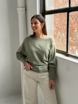 Sweater de punto color verde oliva, con cuello bote y mangas murciélago. Presenta un diseño de textura acanalada vertical en el frente y puños ajustados.
