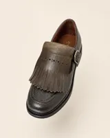 Mocasín de cuero natural color verde musgo, con costuras visibles, hebilla lateral metálica y solapa desmontable con flecos.