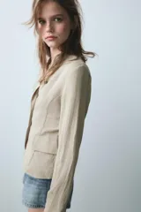Blazer de cuello redondo con escote en pico, manga larga y cierre frontal con botones metálicos. Presenta falsos bolsillos con solapa en el delantero y un diseño estructurado.