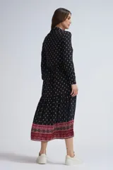 Vestido midi negro con estampado de cachemir en blanco y rojo. Tiene cuello camisero, mangas largas con puños abotonados, cierre frontal con botones y falda escalonada con volantes.
