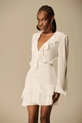 Vestido corto de chiffon color blanco marfil, con escote en V profundo adornado con volados, mangas largas fluidas y falda corta con capas y volados.