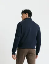 Cardigan de punto color marrón, con cuello alto y cierre frontal completo. Presenta mangas largas tipo ranglan y bolsillos laterales de ribete.