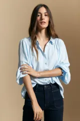 Camisa de manga larga color celeste, con cuello clásico, cierre frontal con botones y puños elastizados con volados. Presenta un diseño fluido con detalle de vainilla en la espalda.