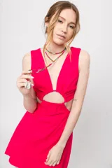 Vestido corto fucsia con escote en V y corte a la cintura. Presenta aberturas laterales y lazo ajustable en la espalda.