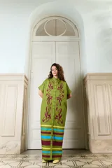 Vestido largo verde militar de popelina de algodón, con diseño oversized, cuello mao, mangas cortas, bolsillos laterales y cierre frontal con botones. Presenta un estampado de flores grandes en la parte superior y franjas horizontales de colores en el ruedo.