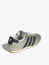 Championes Adidas Taekwondo Lace de perfil bajo, con exterior de cuero metalizado en color plateado y las icónicas tres tiras laterales en color negro. Presenta un diseño acolchado en la puntera y suela plana de goma.