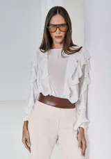 Camisa de color off-white con volados frontales, mangas largas con puños ajustados y diseño fluido de estilo romántico.