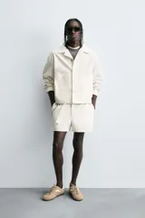 Shorts de algodón color blanco roto, de corte regular fit, con cintura ajustable mediante cinturón del mismo tejido y hebilla metálica. Presenta bolsillos delanteros y bolsillos traseros de vivo.