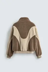 Cazadora de corte relajado confeccionada en tejido de borreguillo con diseño de paneles en tonos marrón y beige. Presenta cuello subido, cierre frontal de cremallera, bolsillos laterales y acabados en rib en puños y cintura.