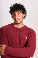 Sweater de punto grueso con cuello redondo y manga larga. Presenta un diseño de tejido acanalado y el logo de la marca bordado en el pecho.