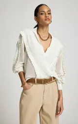 Sweater calado de punto color blanco, de corte recto con amplio cuello tipo polo y escote en V. Presenta mangas largas con volumen, puños ajustados y detalles de volados texturizados en la parte delantera y en las mangas.