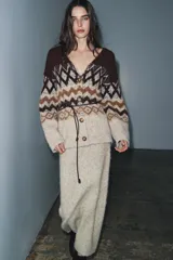 Chaqueta de punto con escote en pico y manga larga, confeccionada en tejido jacquard con diseño geométrico. Presenta detalles de lentejuelas y abalorios, cierre frontal con botones y un cinturón fino ajustable en la cintura.
