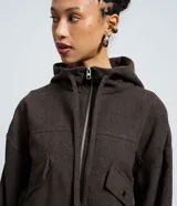 Campera tipo bomber color marrón oscuro, con capucha, cierre frontal de cremallera, bolsillos delanteros con solapa y puños elásticos.