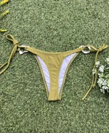 Conjunto de bikini color verde oliva (pistacho) compuesto por un corpiño triangular con argolla central y una bombacha colaless con tiras laterales ajustables y argollas laterales. Las argollas son de zamak.