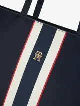 Cartera tipo tote de Tommy Hilfiger en color azul marino, con diseño de franjas verticales en el centro en tonos blanco, azul y rojo. Presenta logo metalizado dorado en la parte frontal y doble asa superior.