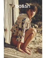 Sweater de punto beige con capucha y cordones burdeos. Presenta un diseño jacquard con motivos geométricos en azul, amarillo y rojo.