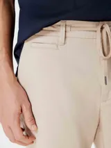 Bermuda de gabardina color beige con cintura elástica y cordón ajustable. Presenta bolsillos laterales y ruedo con dobladillo.