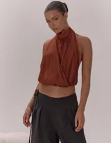 Top de escote halter con cuello alto, diseño frontal cruzado con pliegues y espalda descubierta con lazo regulable. Presenta una terminación elasticada en la cintura y está confeccionado en una tela liviana con caída fluida.