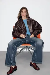 Cazadora estilo bomber de efecto piel en color bordó, con cuello solapa, manga larga, bolsillos delanteros de vivo con botón a presión y bajo elástico. Cierre frontal con cremallera oculta y botones a presión.