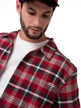 Camisa de manga larga con estampado de cuadros en tonos rojos, negros y blancos. Presenta cuello camisero, cierre frontal con botones, puños abotonados y un bolsillo en el pecho con etiqueta de la marca.