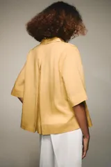 Camisa de color mostaza, con cuello solapa, manga corta y bajo recto. Cierre frontal con botones.