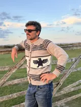 Sweater de punto con diseño artesanal, cuello redondo y cierre frontal con botones. Presenta un patrón de franjas horizontales con un motivo central de águila en color oscuro sobre fondo claro.