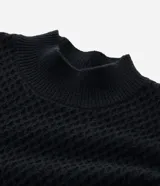 Buzo de punto negro con textura geométrica tipo colmena, cuello alto y mangas largas con puños ajustados.