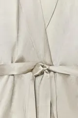 Blazer color plateado confeccionada en hilatura con mezcla de viscosa y lino. Tiene cuello solapa de muescas, manga larga y cinturón en mismo tejido ajustable con lazadas.